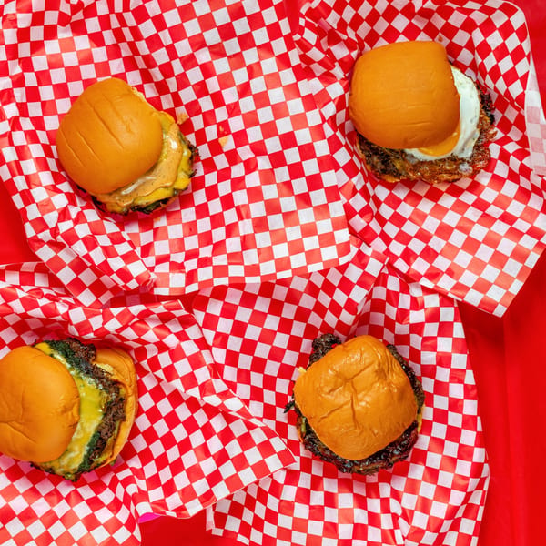 Four Ban Ban Burgers, two with cheese and sauce, one with a fried egg, on red checkered paper.
