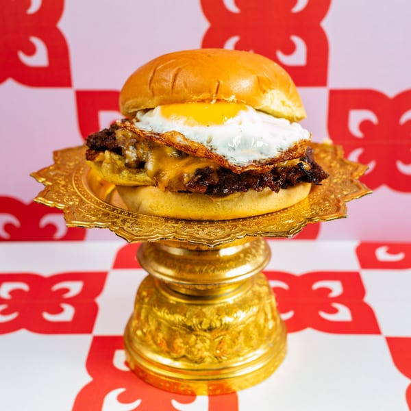 Ban Ban Burger with a fried egg and melted cheese on a golden pedestal against a red and white background.
