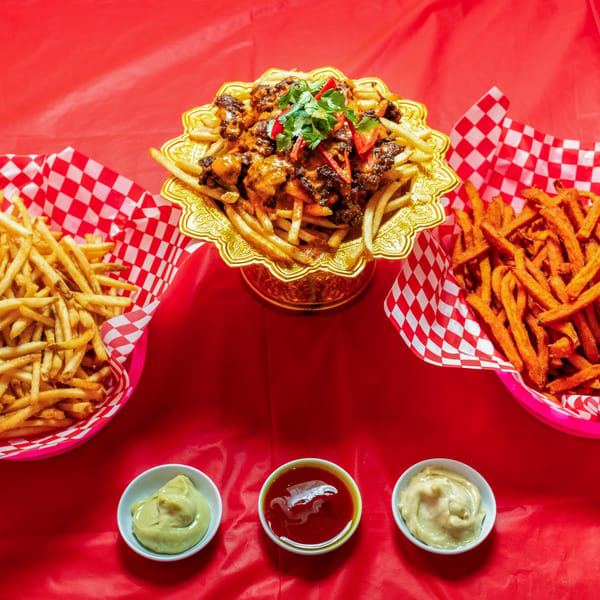 Ban Ban Burger's chili cheese fries, regular fries, and sweet potato fries with dipping sauces on a red background.