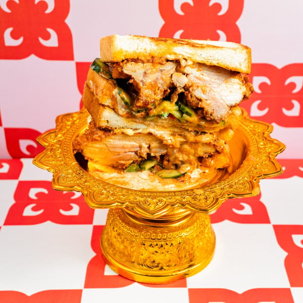 A Ban Ban Burger with crispy chicken, sauce, and pickles on a golden pedestal against a red and white background.