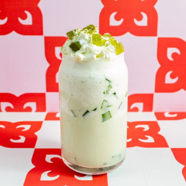 Matcha drink with whipped cream and green jelly cubes on a red and white checkered background.
