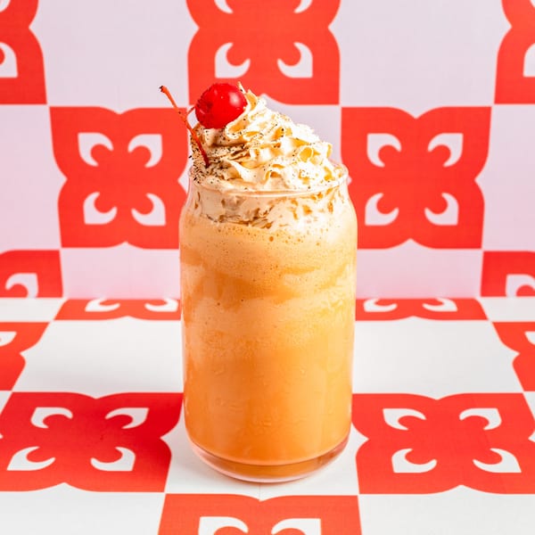 Ban Ban Burger's orange milkshake with whipped cream and a cherry on a red and white patterned background.
